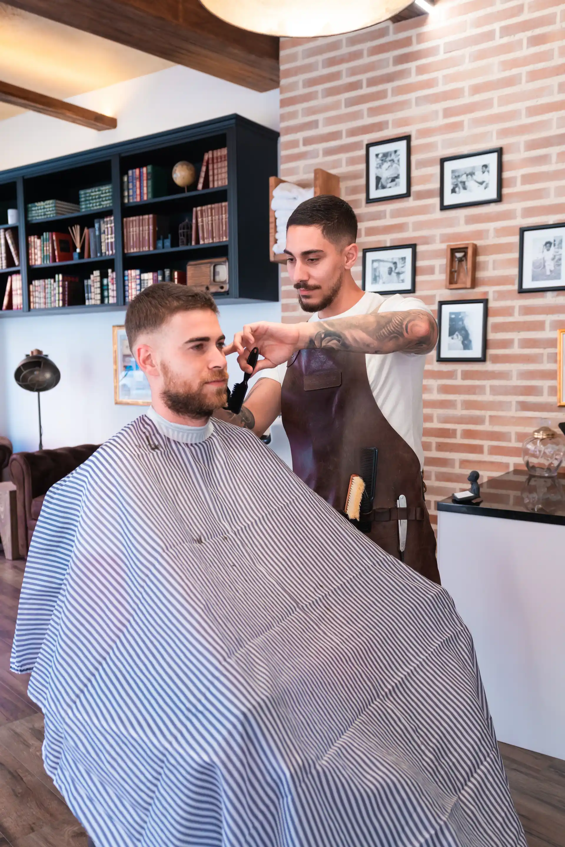 Foto vertical de barbería — barbero cortando cabello con tijeras a cliente frente a espejo, estética vintage.