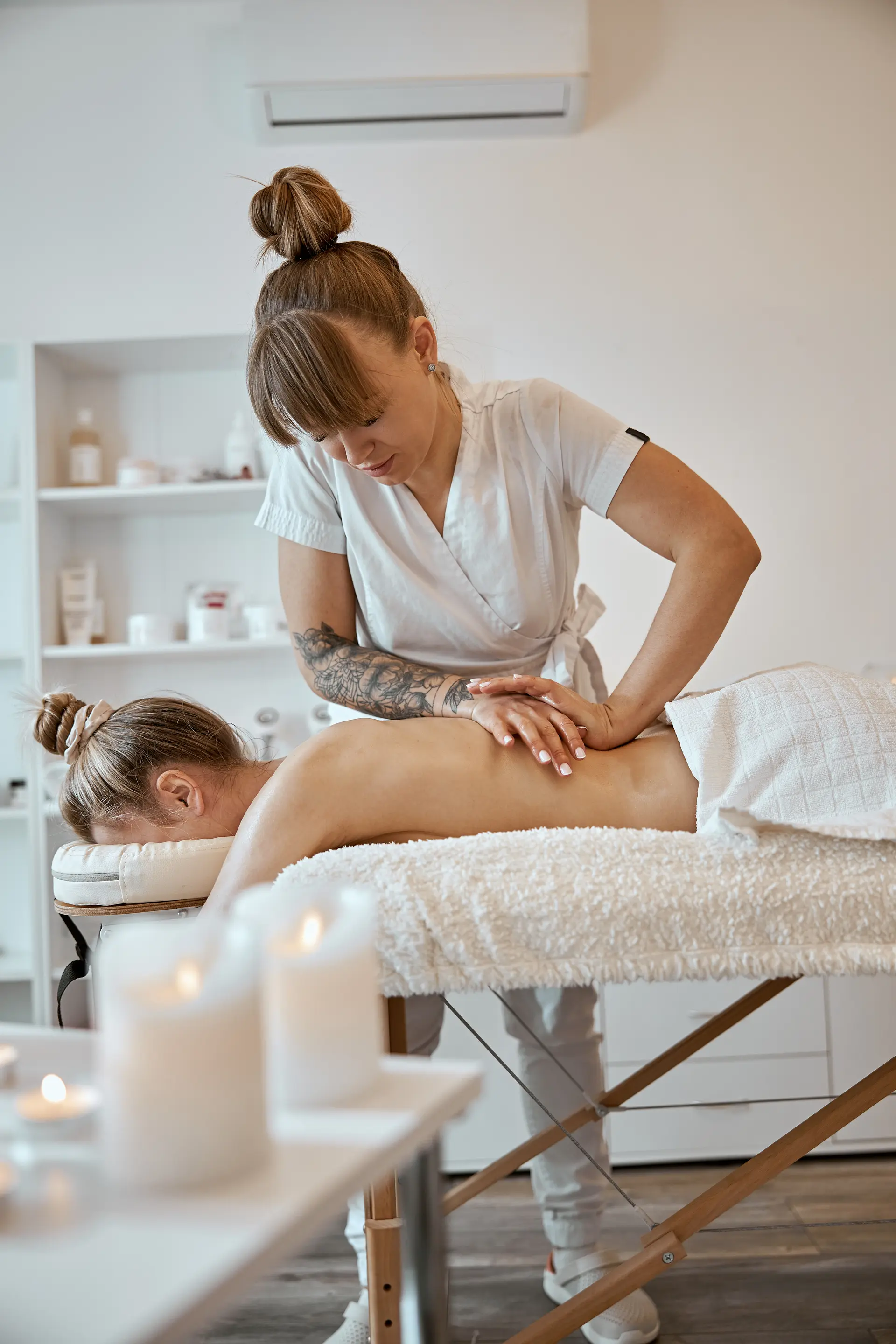 Foto vertical de camilla de masajes — manos de terapeuta trabajando sobre espalda de cliente, ambiente sereno.